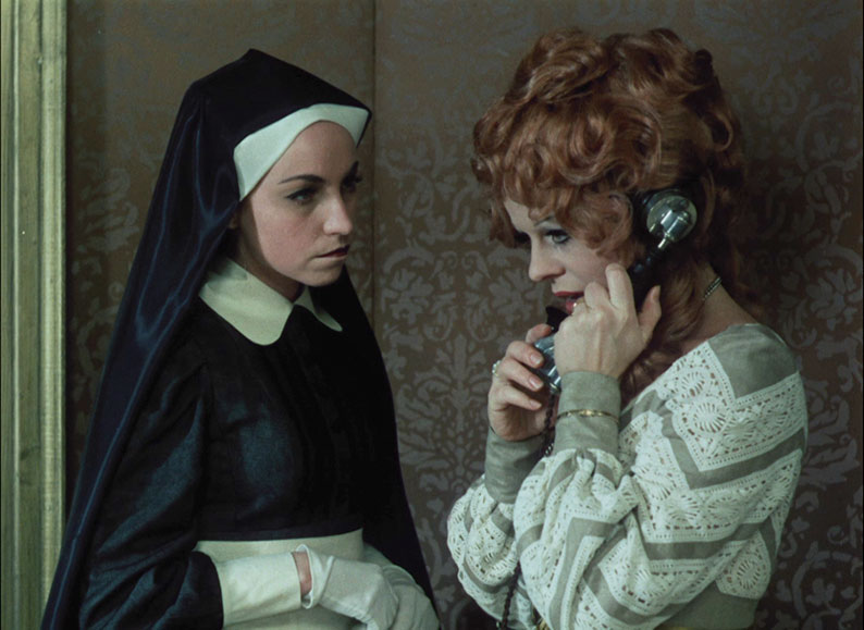 Klára takes a phone call while her stern nurse looks on